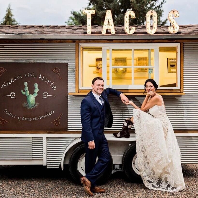 A couple standing in front of a taco food truck holding hands